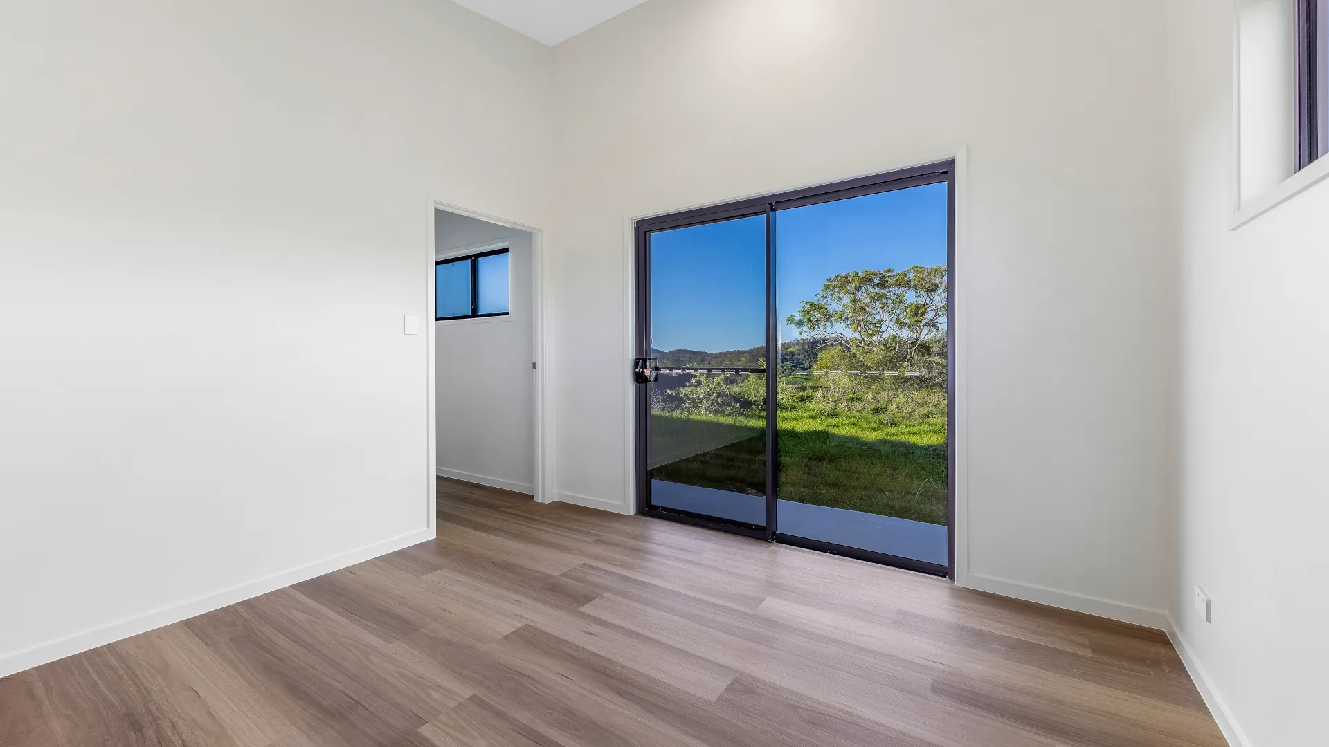 Bright bedroom with sliding glass doors overlooking a green Beerwah hinterland property